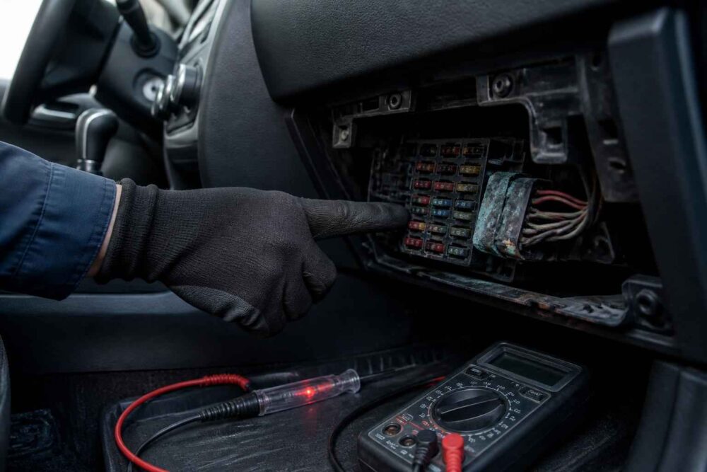 Sprawdzanie skrzynki bezpieczników w samochodzie Mechanik wskazuje bezpiecznik w samochodowej skrzynce, obok leży multimetr i próbnik napięcia